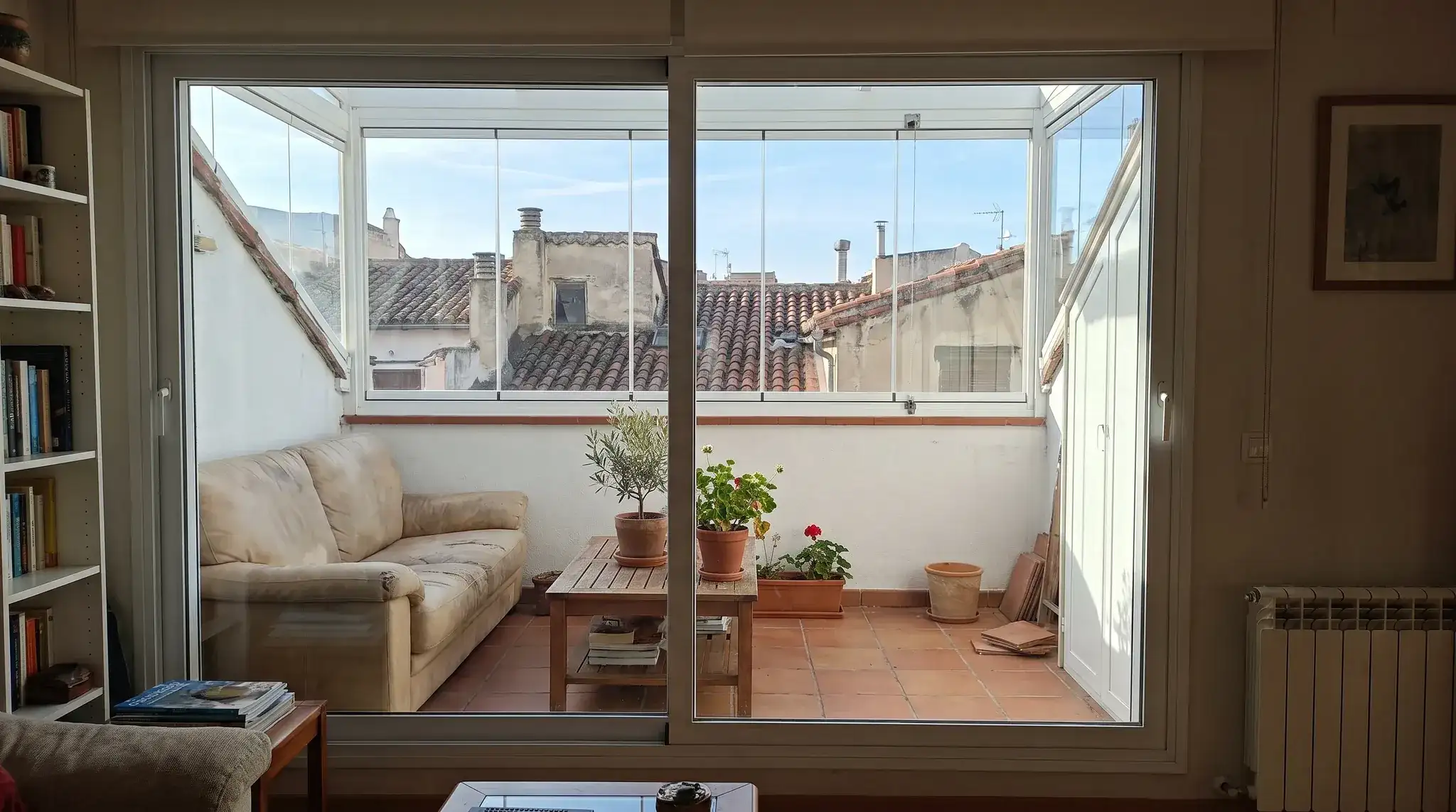 Terraza de ático cerrada con cristal, con sofá y plantas, vista desde el salón