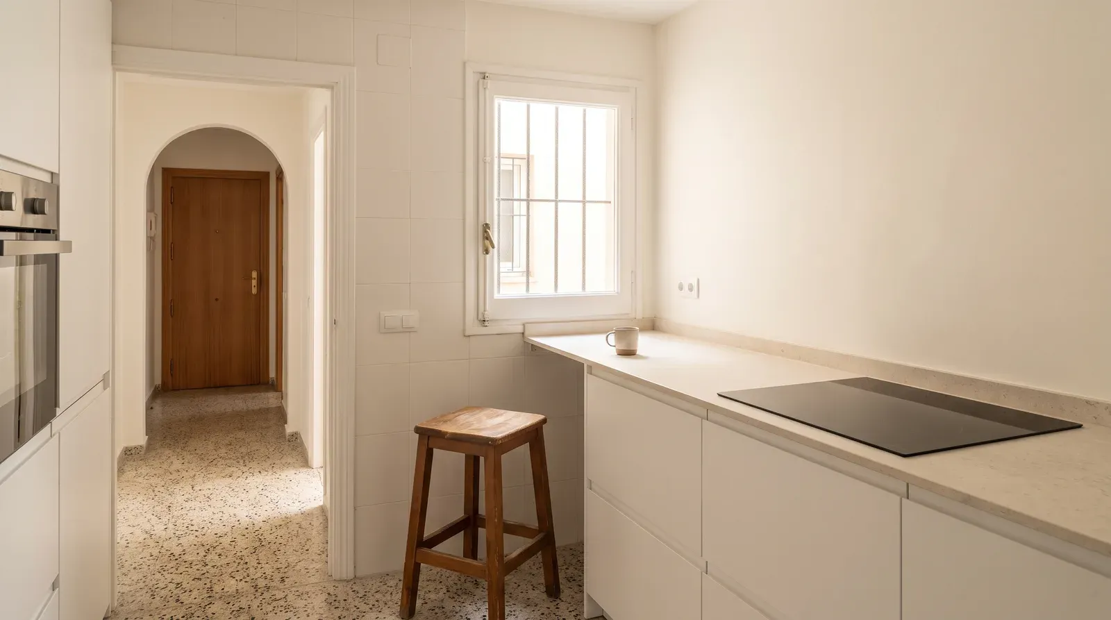 Cocina reformada con muebles blancos, encimera clara y placa de inducción en un piso de Madrid